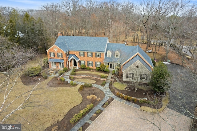 view of front of house with decorative driveway, a chimney, and brick siding