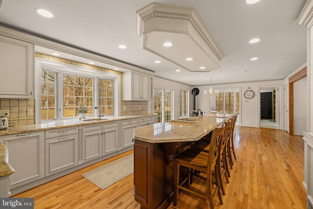 kitchen featuring a chandelier, light wood-style flooring, a sink, decorative backsplash, and light stone countertops