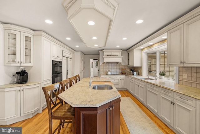 kitchen featuring black appliances, a kitchen bar, light wood finished floors, and a sink