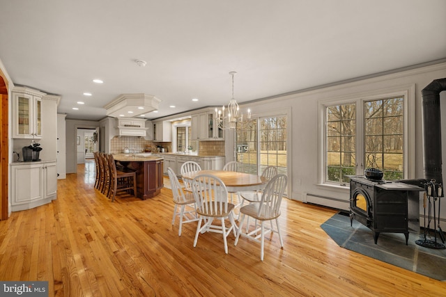 dining space featuring crown molding, a baseboard radiator, recessed lighting, light wood-style flooring, and a wood stove