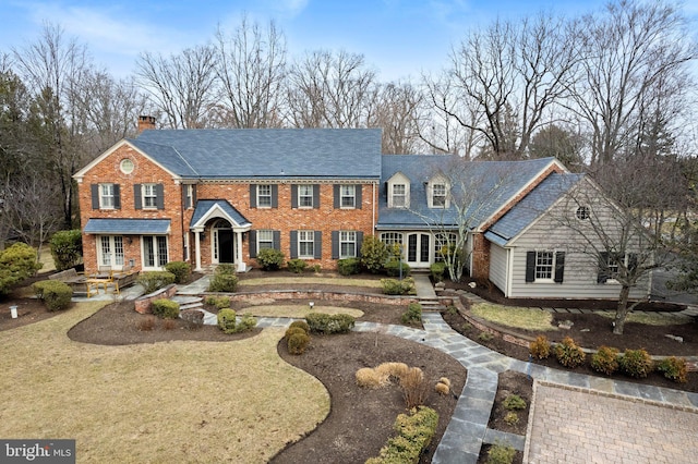 colonial-style house with a front yard, french doors, brick siding, and a chimney