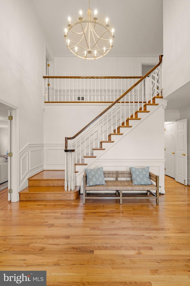 staircase featuring ornamental molding, wainscoting, a high ceiling, and wood finished floors