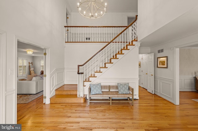 stairs with wainscoting, visible vents, wood finished floors, and ornamental molding