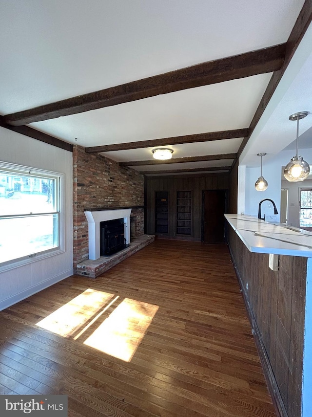 unfurnished living room featuring dark wood-style flooring, a fireplace, a sink, and beam ceiling