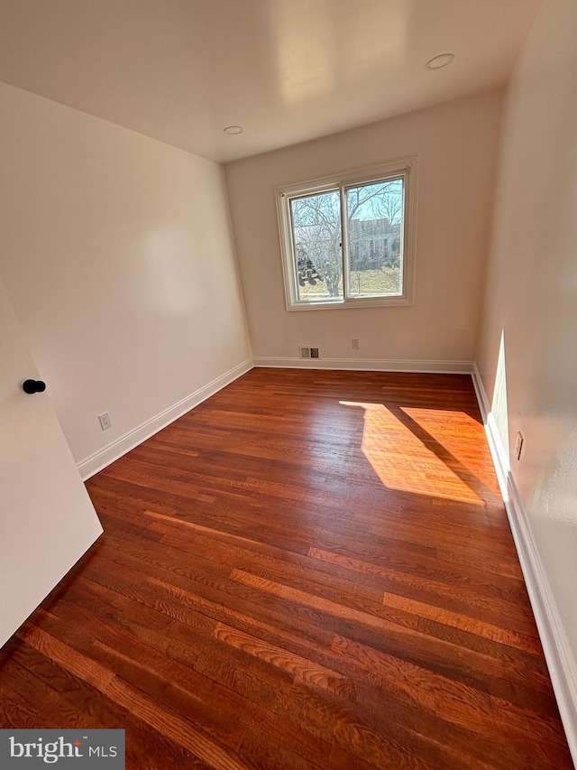 unfurnished room featuring baseboards, visible vents, and dark wood finished floors