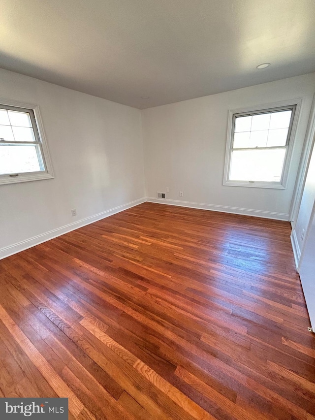 unfurnished room featuring baseboards, dark wood-style flooring, and a healthy amount of sunlight