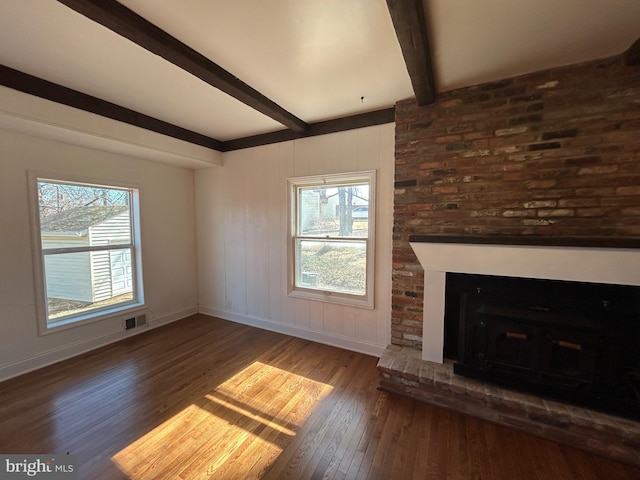 unfurnished living room with a healthy amount of sunlight, visible vents, beamed ceiling, and wood-type flooring