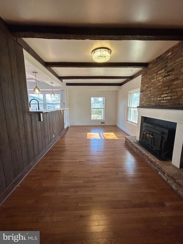 unfurnished living room featuring dark wood-style floors, wooden walls, a fireplace, and beamed ceiling