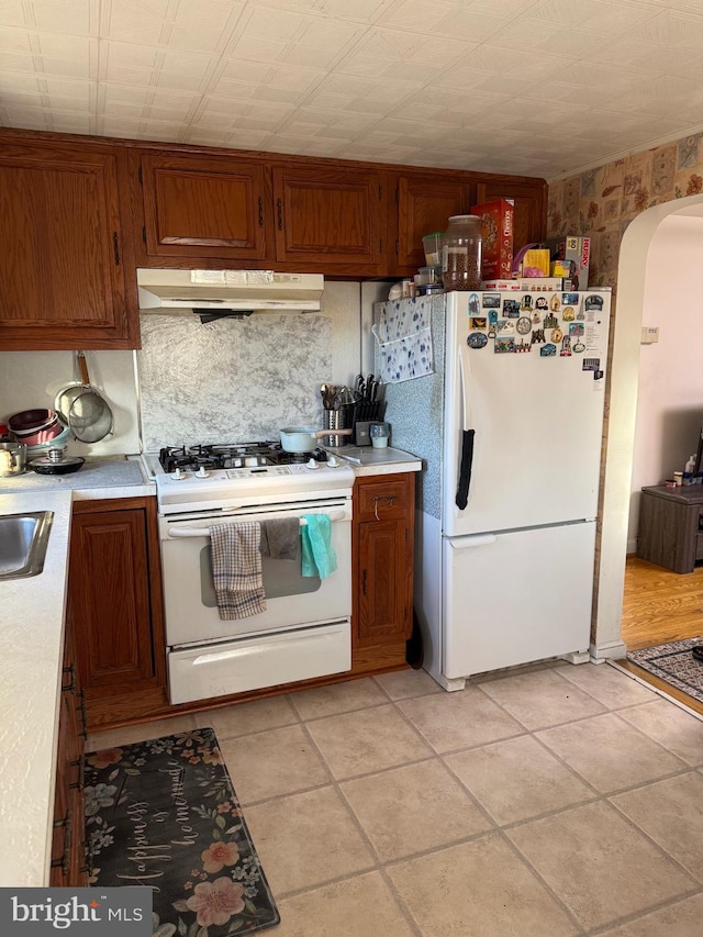 kitchen with arched walkways, white appliances, light countertops, and under cabinet range hood