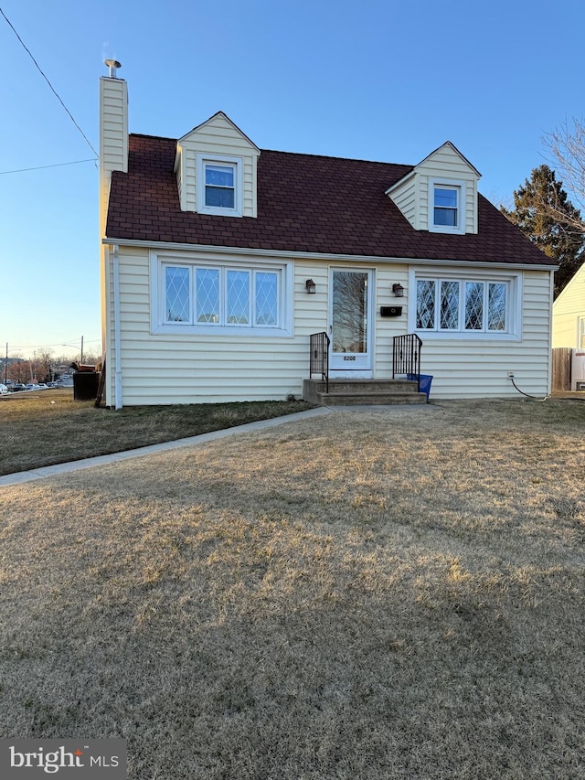 new england style home with a front lawn, a chimney, and a shingled roof