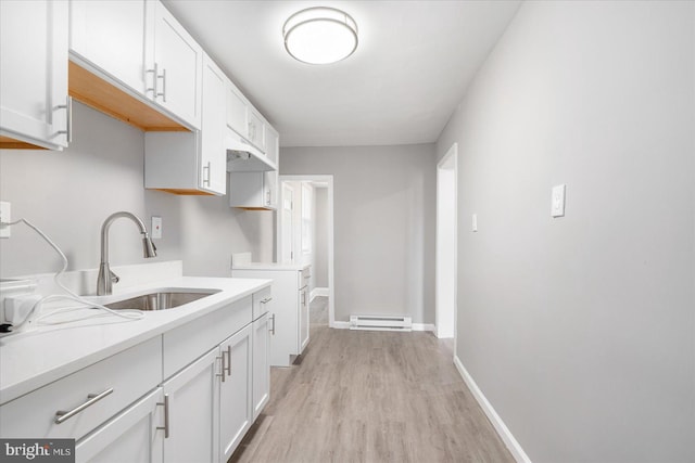 kitchen featuring a sink, baseboards, light countertops, baseboard heating, and light wood finished floors