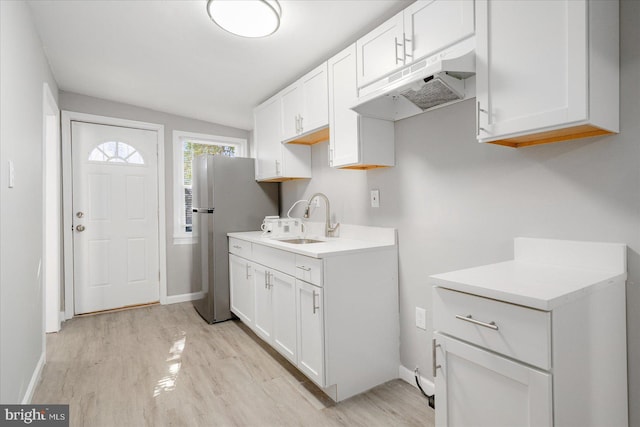 kitchen featuring under cabinet range hood, a sink, white cabinets, light wood-style floors, and freestanding refrigerator