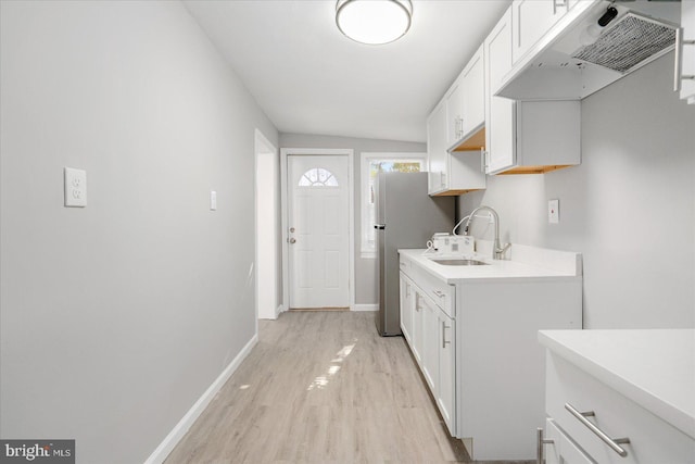 kitchen featuring under cabinet range hood, a sink, baseboards, light countertops, and light wood finished floors