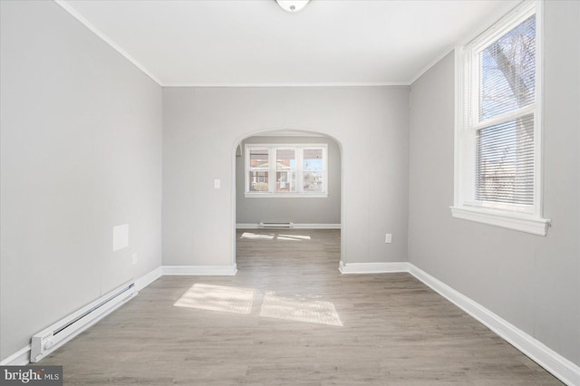 empty room featuring arched walkways, a baseboard radiator, wood finished floors, and baseboards