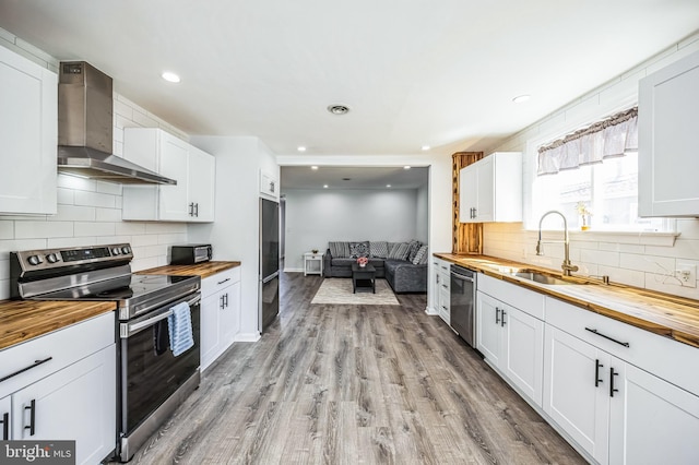 kitchen featuring butcher block countertops, stainless steel appliances, light wood-style floors, and wall chimney range hood