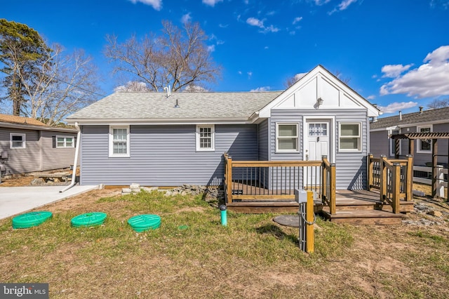 rear view of property with a deck, roof with shingles, and a lawn