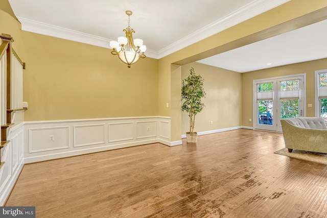 interior space with light wood-style floors, a chandelier, wainscoting, and crown molding