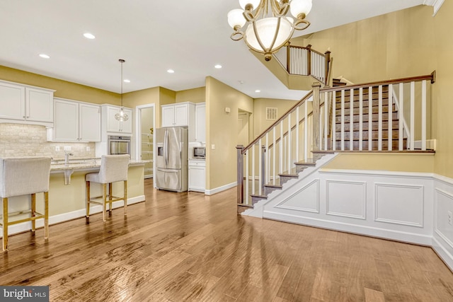 interior space with stainless steel appliances, white cabinetry, a kitchen breakfast bar, light wood-style floors, and backsplash