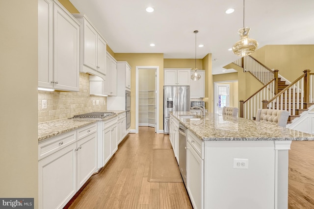 kitchen with decorative backsplash, light wood-style floors, appliances with stainless steel finishes, white cabinetry, and a sink