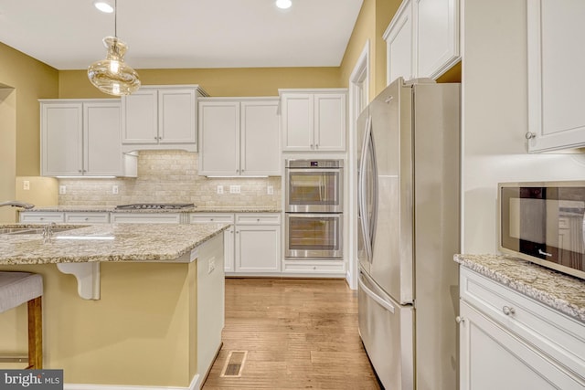 kitchen with visible vents, decorative backsplash, stainless steel appliances, white cabinetry, and a sink