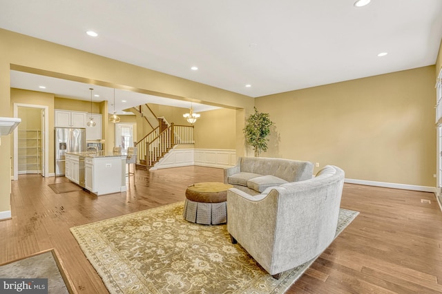 living area with light wood-style flooring, recessed lighting, baseboards, stairway, and an inviting chandelier