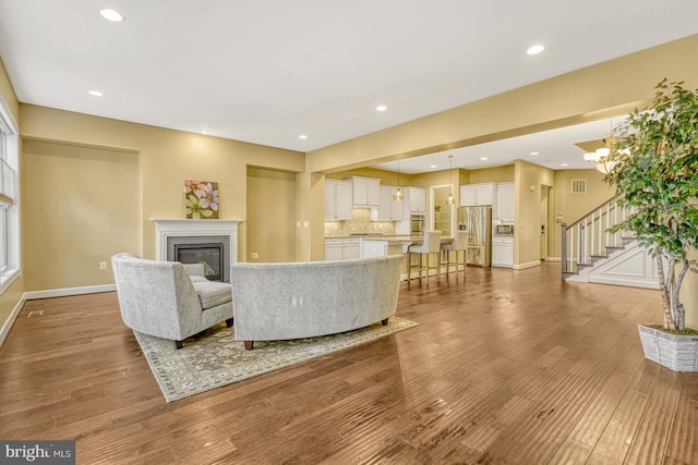 living area with wood finished floors, stairway, a glass covered fireplace, and baseboards