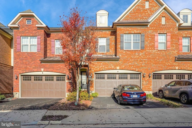 townhome / multi-family property with driveway, a standing seam roof, metal roof, and brick siding