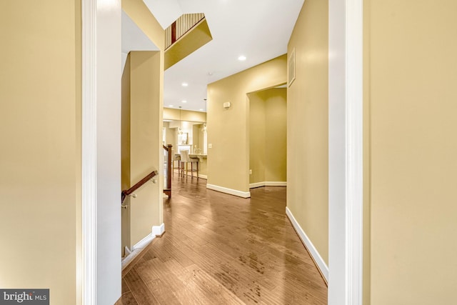 corridor with recessed lighting, baseboards, wood finished floors, and an upstairs landing