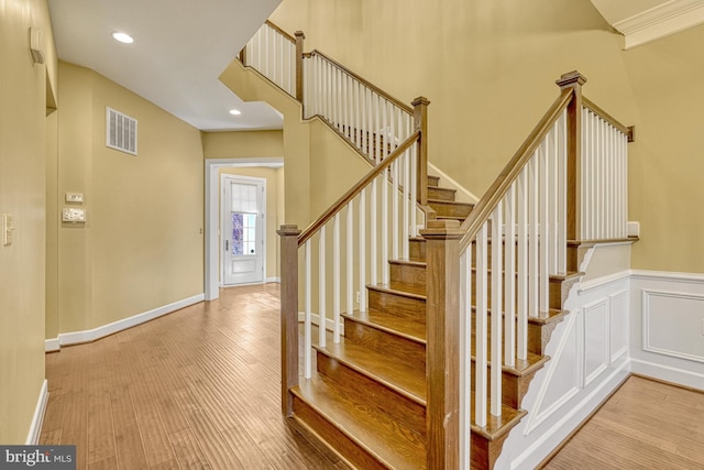 stairway featuring recessed lighting, visible vents, a decorative wall, wainscoting, and wood finished floors