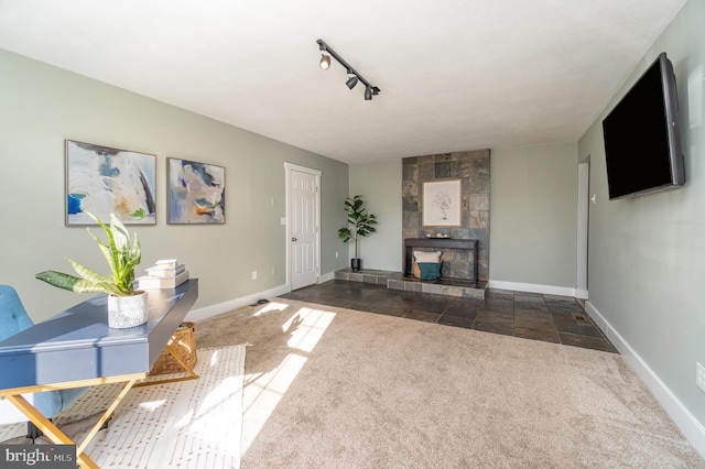 unfurnished living room featuring track lighting, dark colored carpet, baseboards, and a tiled fireplace