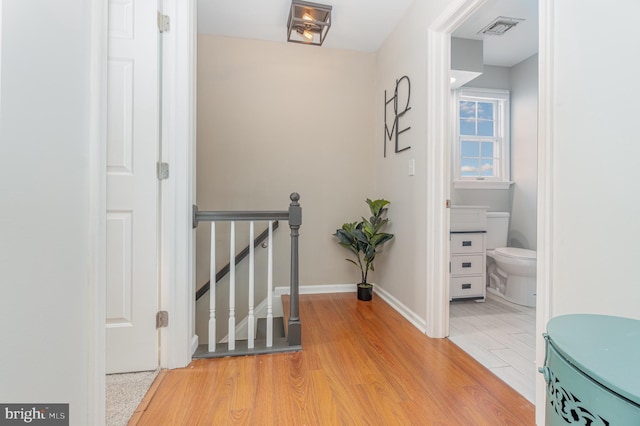 corridor with light wood finished floors, an upstairs landing, visible vents, and baseboards