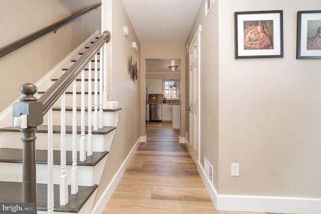 hallway with visible vents, light wood-style flooring, and baseboards