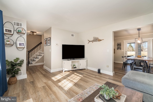 living room with light wood-style flooring, visible vents, stairway, and baseboards