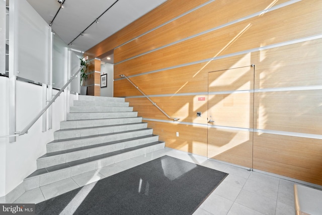 stairway with rail lighting, wood walls, and tile patterned floors