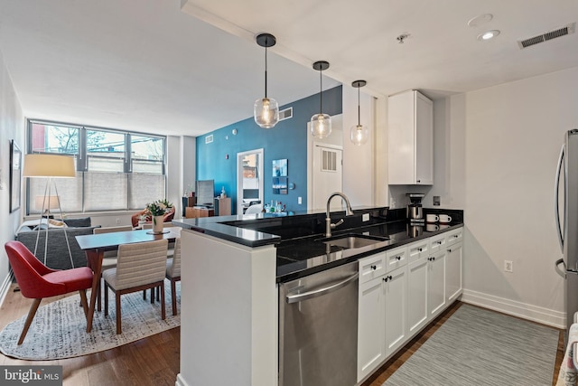 kitchen with dark countertops, visible vents, appliances with stainless steel finishes, a sink, and a peninsula