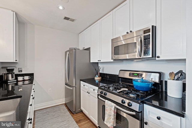 kitchen featuring stainless steel appliances, visible vents, baseboards, white cabinets, and light wood-type flooring