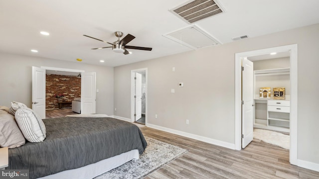 bedroom featuring a walk in closet, visible vents, attic access, light wood-style floors, and baseboards