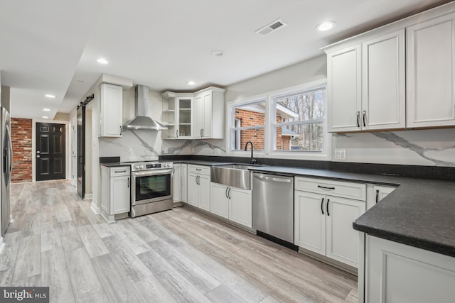 kitchen with a barn door, visible vents, wall chimney exhaust hood, appliances with stainless steel finishes, and a sink