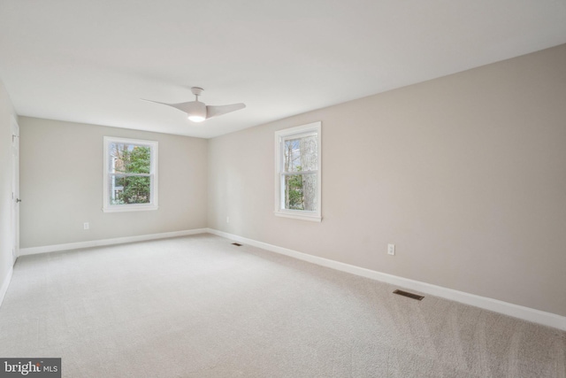 carpeted empty room featuring ceiling fan, plenty of natural light, visible vents, and baseboards