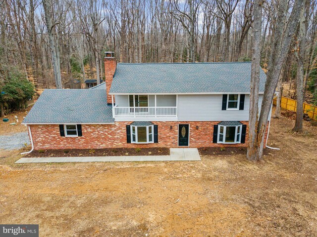 view of front of property featuring a balcony, roof with shingles, a chimney, and brick siding