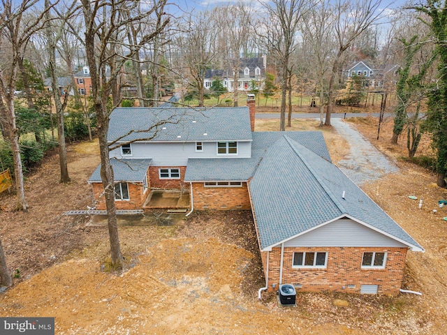 exterior space with roof with shingles, brick siding, a chimney, and central air condition unit