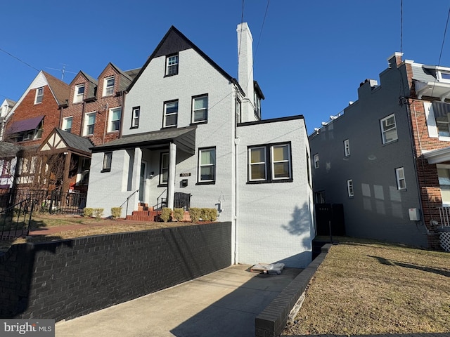 view of front of property featuring a residential view, brick siding, a chimney, and fence