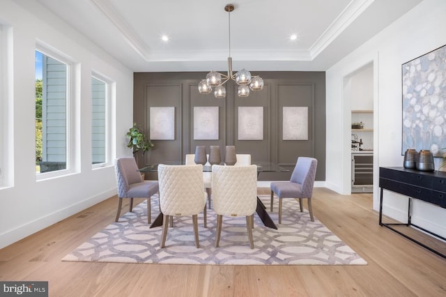 dining area with light wood-type flooring, an inviting chandelier, ornamental molding, and a raised ceiling