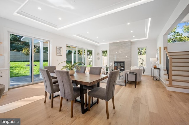 dining room with plenty of natural light, light wood-style flooring, stairs, and a raised ceiling