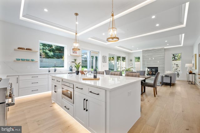 kitchen with a tray ceiling, a fireplace, open shelves, white cabinetry, and light wood-type flooring