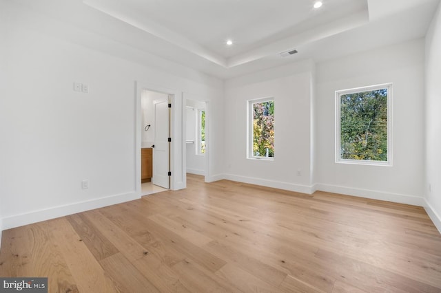 unfurnished room with a tray ceiling, light wood-style flooring, and baseboards