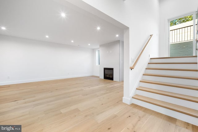 unfurnished living room featuring a large fireplace, light wood-style flooring, stairs, and recessed lighting