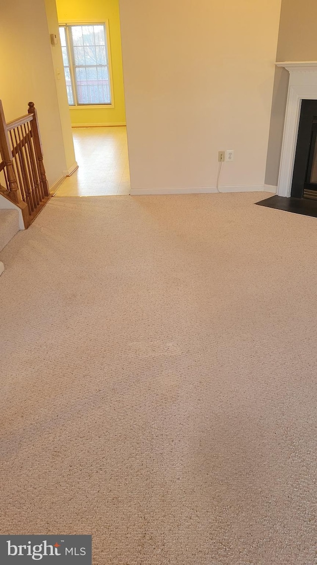 unfurnished living room featuring a fireplace with flush hearth and carpet