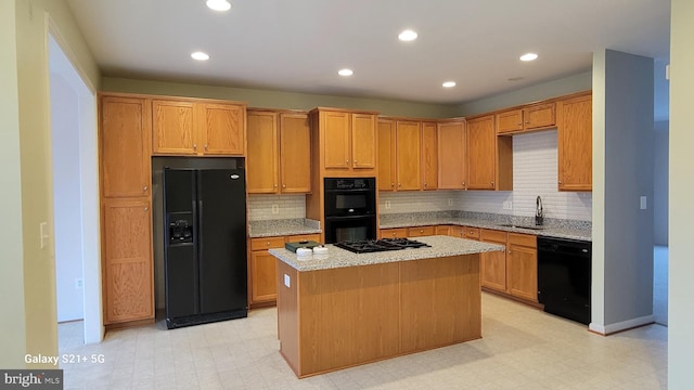 kitchen with light stone counters, light floors, a sink, a center island, and black appliances