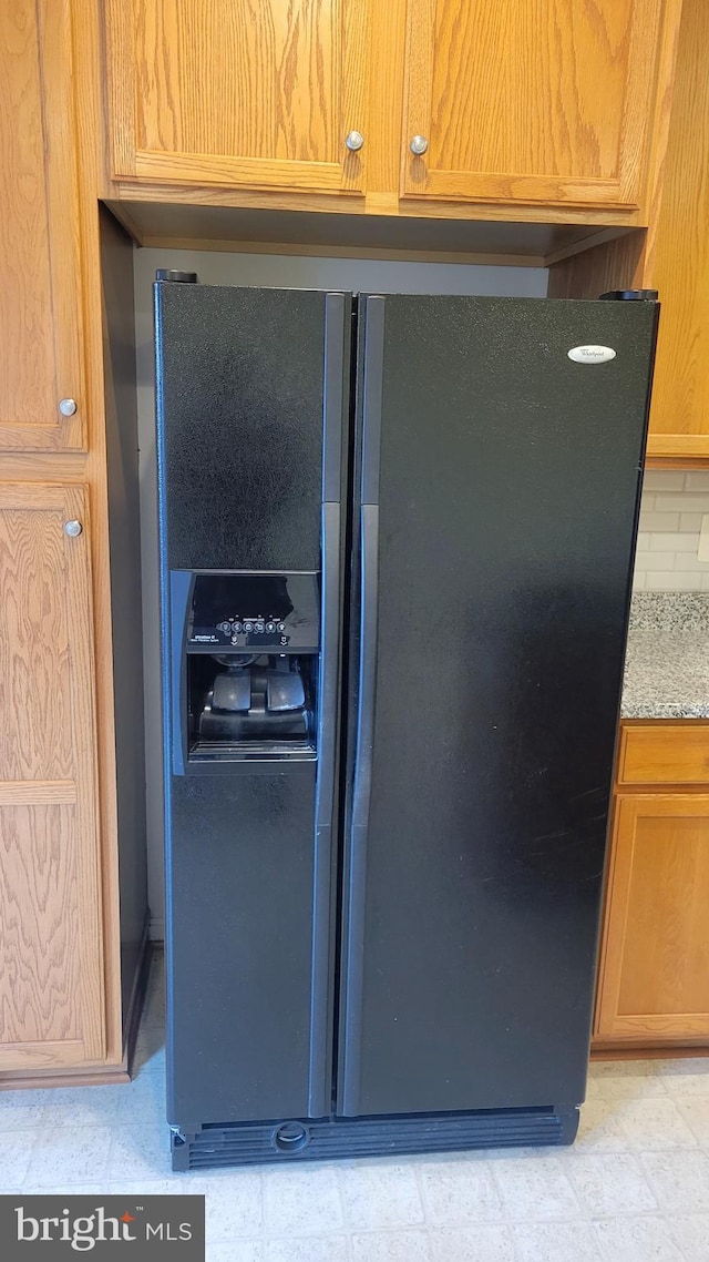 interior details featuring light stone counters, backsplash, and black fridge with ice dispenser